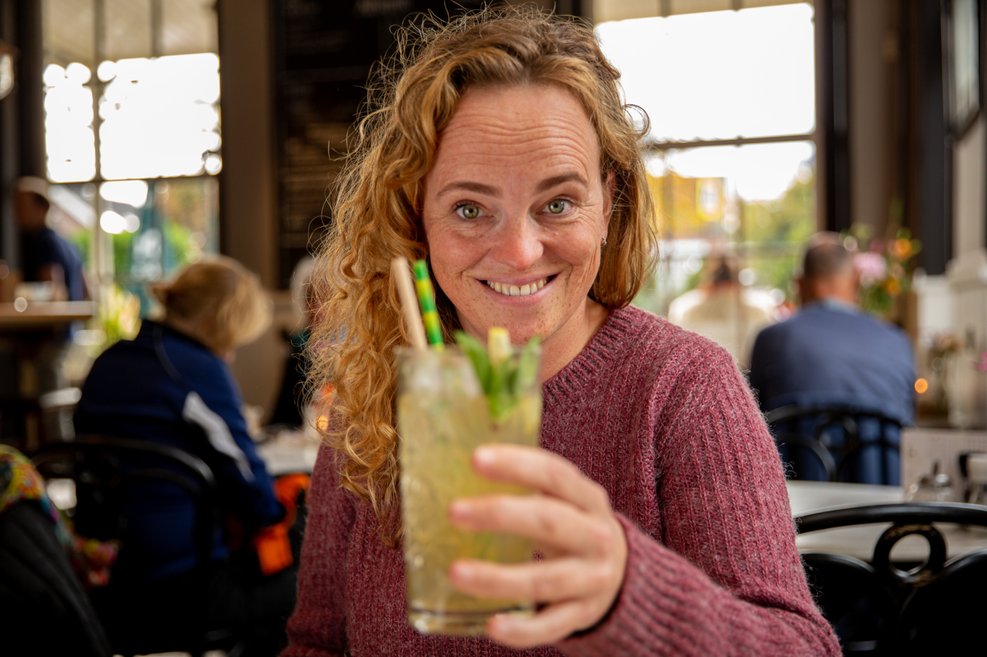 Een vrolijk kijkende dame die proost met een ijsthee van De Eendracht